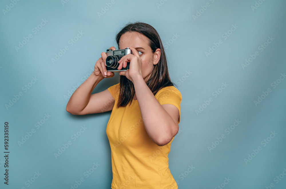 A woman takes pictures with an old film camera. Yellow boot cap, black hair, blue background A woman takes pictures with an old film camera. Yellow boot cap, black hair, blue background