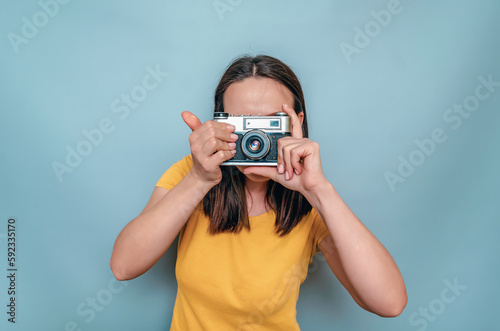 Woman takes pictures with an old film camera. Yellow boot cap, black hair, blue background