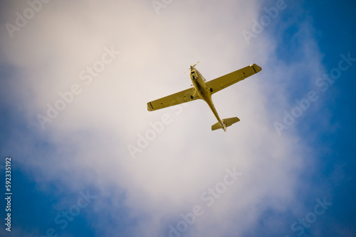 One-engine plane flying under white cloud in blue sky