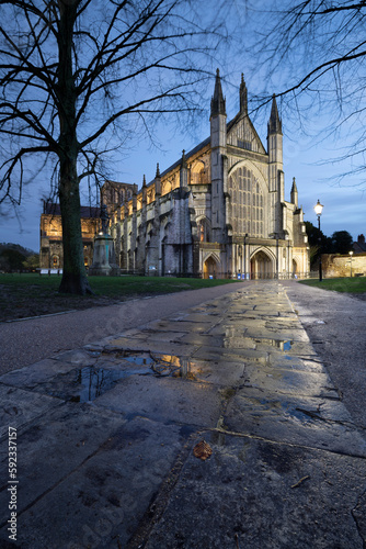 Winchester Cathedral floodlit at night in winter with reflections on wet pavement in foreground, Winchester, Hampshire