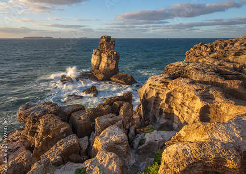 Waves crashing against rock stack at Cabo Carvoeiro in evening sunlight with Ilha da Berlenga in the distance, Peniche, Centro Region, Estremadura, Portugal photo