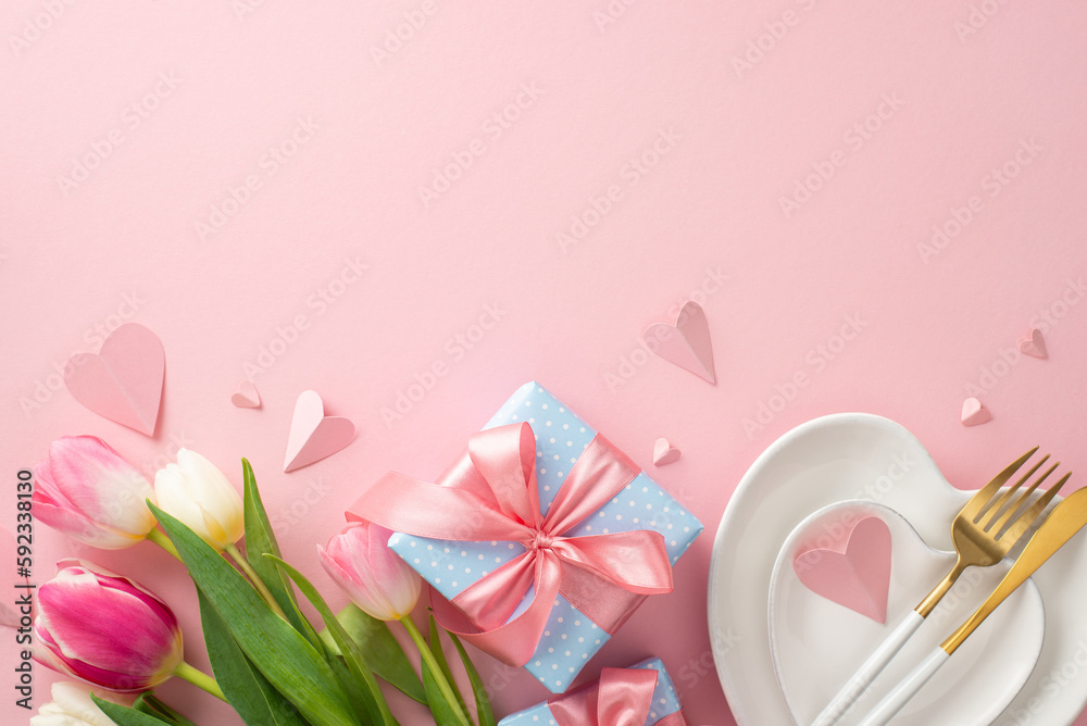 Festive Mother's day table arrangement. Top view flat lay of plates, cutlery, tulips, gift boxes, and decorative hearts on pastel pink background with a space for promotional content or text