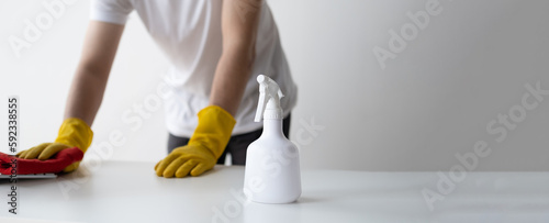Close up view of man cleaning white wooden table using clothes and cleaning solution liquid spray.