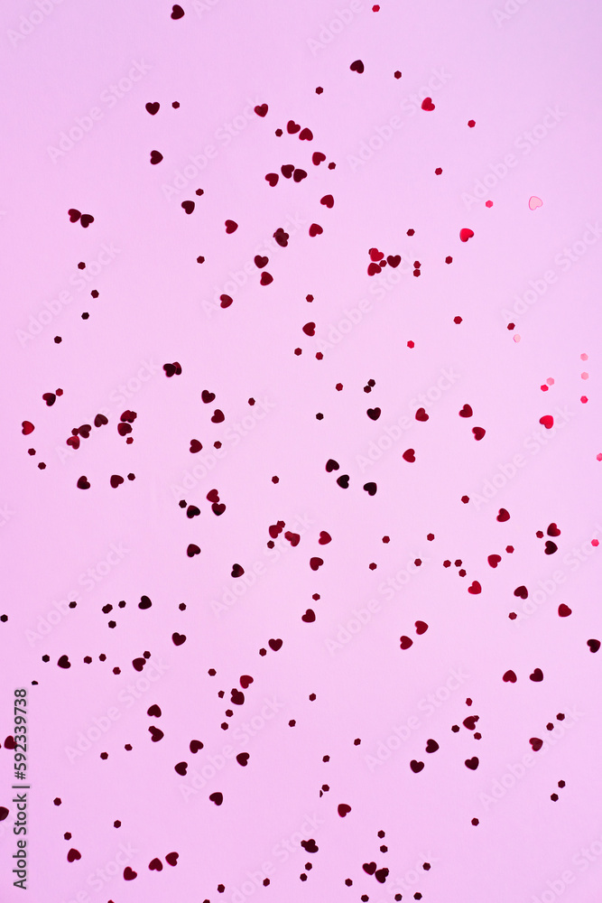 Many small red hearts on a pink background. Holiday concept. Flat lay for your design. Vertical image.
