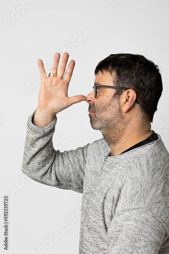 Man in profile wearing gray sweater. Brings right hand to nose and grimaces