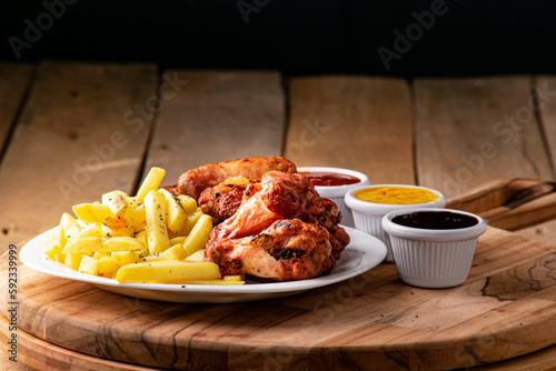bbq chicken wings with french fries and ketchup, mustard and bbq on a rustic wooden table on a black background