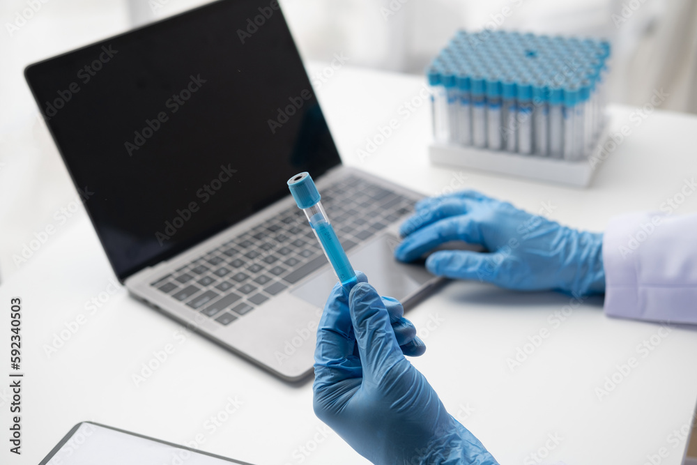 Doctor holds test tube and using on laptop. entering test results into the database. Doctor holds test tube and using on laptop. entering test results into the database.