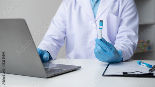 Doctor holds test tube and using on laptop. entering test results into the database.