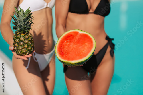 Summer pool party portrait of two best friends girls, standing and holding tasty exotic fruits, health vegan lifestyle, relax, joy