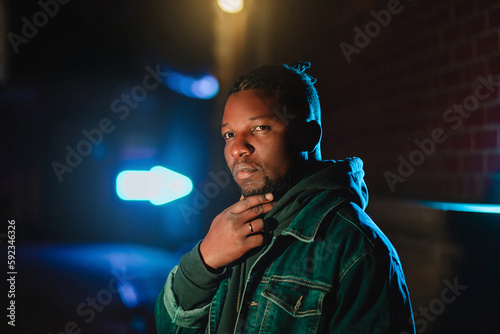 Black man at night in the city among the signs. Photo in the dark. Afro-american man in jacket and bandana.