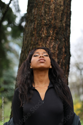 Portrait of an African woman leaning on a tree looks up, environment.