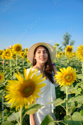 Beautiful young asian woman wear a hat standing and smiling in sunflower blooming garden in sunny day