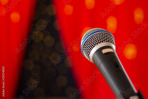 Um microfone preto, em um palco com cortina vermelha desfocada ao fundo. photo