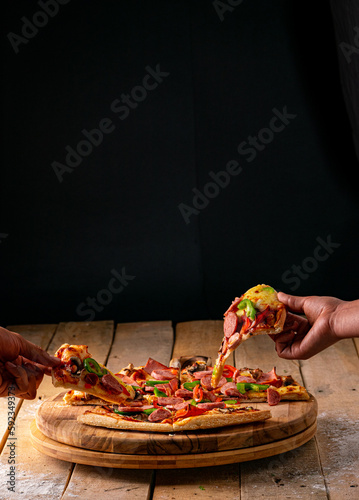 Hands taking a piece of Pizza on a rustic wooden table with a black background