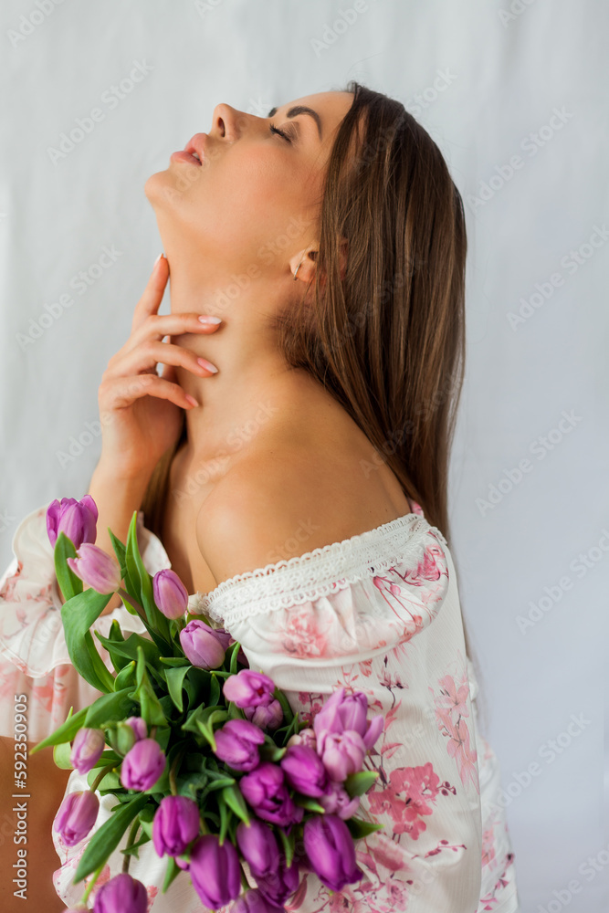 Portrait of sexy beautiful young woman with long hair. Model with a bouquet of lilac tulips on white. Spring. Holidays.
