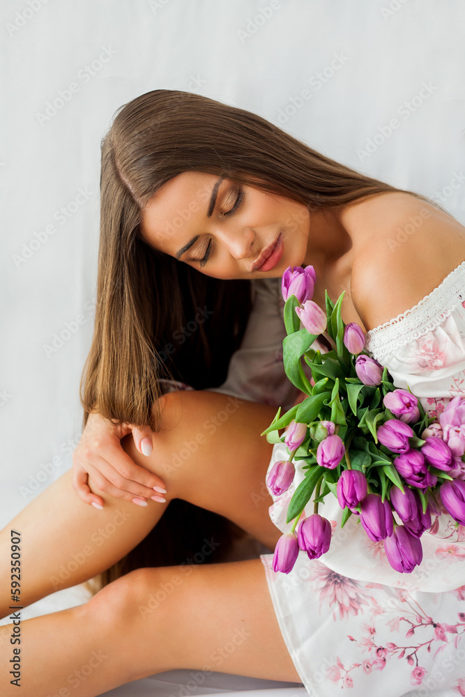 Portrait of sexy beautiful young woman with long hair. Model with a bouquet of lilac tulips on white. Spring. Holidays.