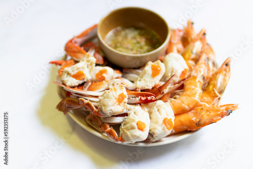 Steamed blue crab legs and shrimp on plate serving with spicy sauce.