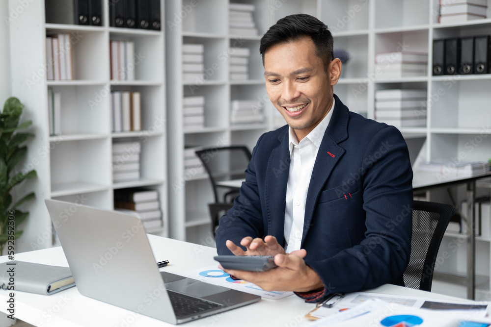 Confident handsome businessman sitting at his desk while using the calculator for the project. Confident handsome businessman sitting at his desk while using the calculator for the project.