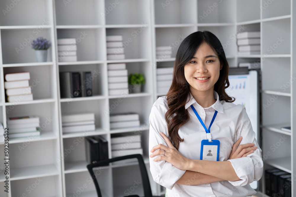 Portrait of young smiling Asian businesswoman looking at camera with crossed arms, standing in the office room. Portrait of young smiling Asian businesswoman looking at camera with crossed arms, standing in the office room.