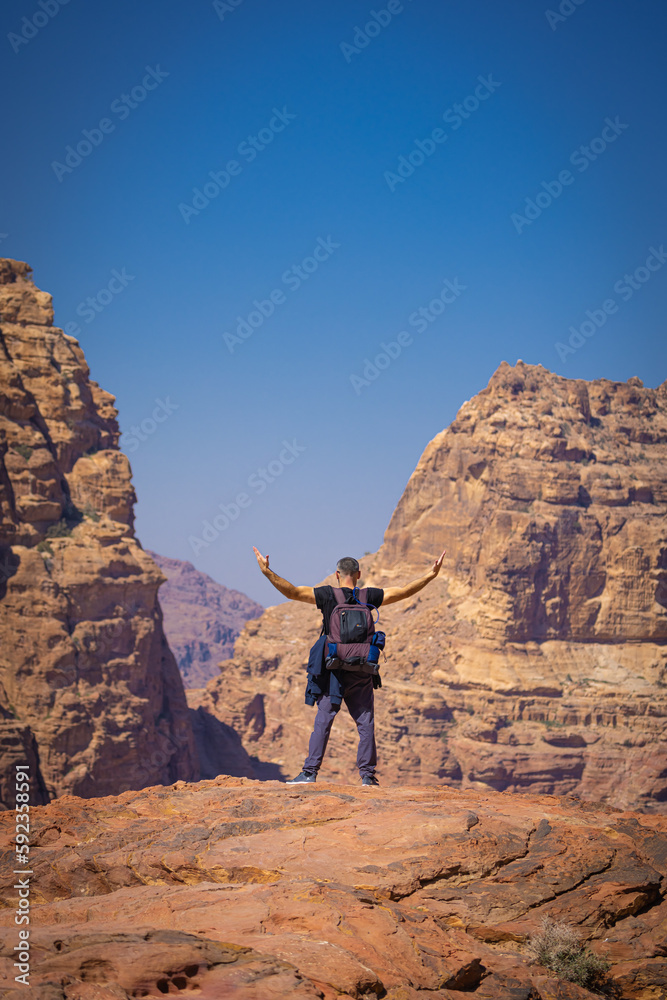 Petra w Jordanii. Mężczyzna stojący na szczycie skalnej góry na tle błękitnego, niebieskiego nieba.  - obrazy, fototapety, plakaty 