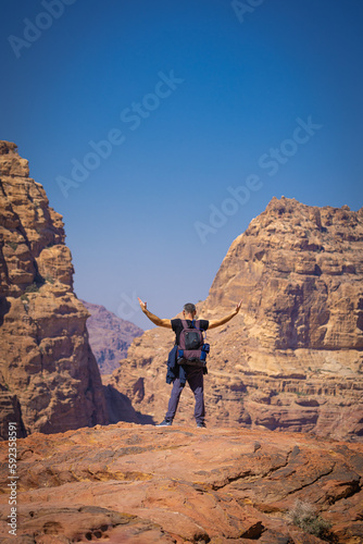 Petra w Jordanii. Mężczyzna stojący na szczycie skalnej góry na tle błękitnego, niebieskiego nieba. 