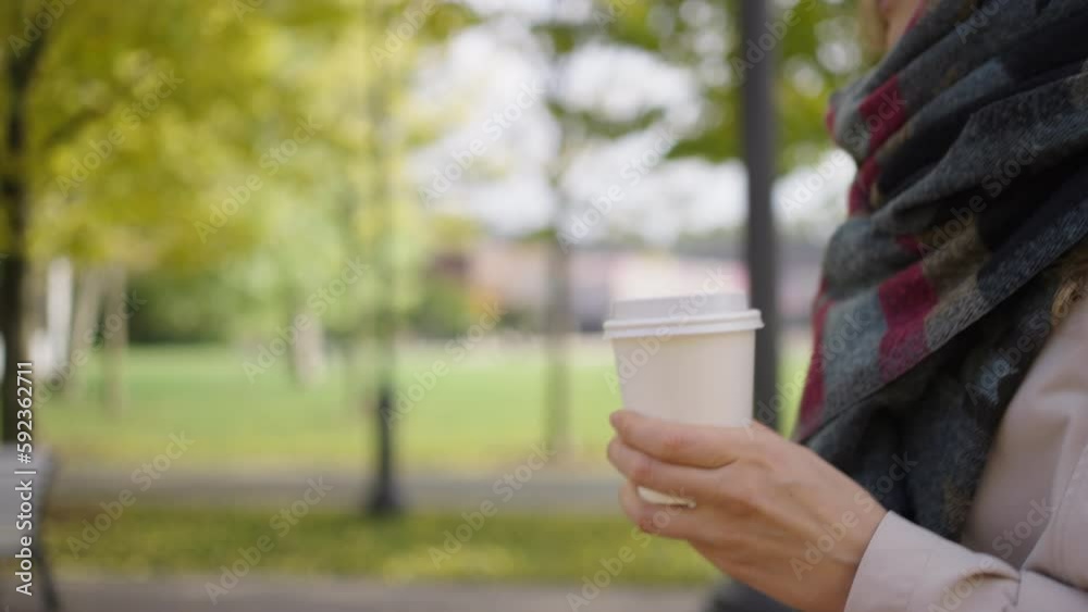 Woman carrying a disposable white cup of coffee or drink to go in the park while walking on a cold summer day close-up