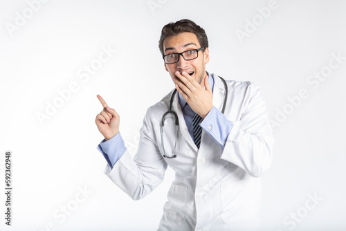 Positive handsome male doctor in medical gown and stethoscope pointing on free space isolated on white background. Copy space and place for text in medical