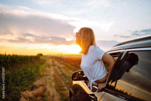 Lifestyle! Happy woman enjoys sunset views from the car window. Young tourist woman rests and leans out of the car window, enjoys the trip. Travel concept, vacation. Towards adventure. © maxbelchenko