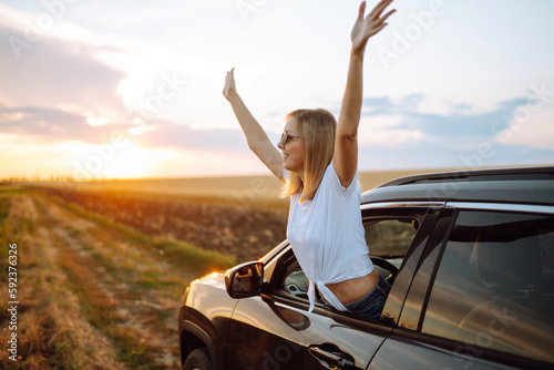 Lifestyle! Happy woman enjoys sunset views from the car window. Young tourist woman rests and leans out of the car window, enjoys the trip. Travel concept, vacation. Towards adventure.