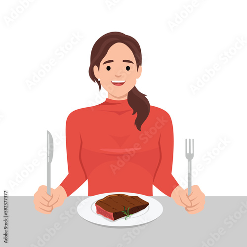 Young woman enjoy eating steak in the dish holding knife and fork as she is ready to eat