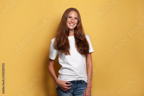 Cheerful mid adult woman in white t-shirt against yellow studio wall background