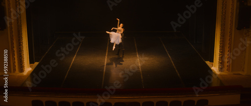 Wide shot of ballet dancers practicing choreography on classic theater stage. Man and woman prepare dance performance. Rehearsal of theatrical show. Art of classical ballet dance. Dramatic lighting.