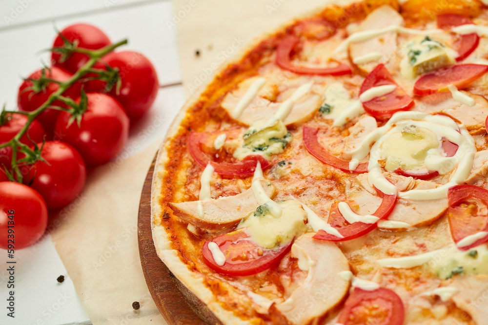 Freshly baked pizza with smoked chicken fillet and gorgonzola cheese served on wooden background with tomatoes, sauce and herbs. Food delivery concept. Restaurant menu