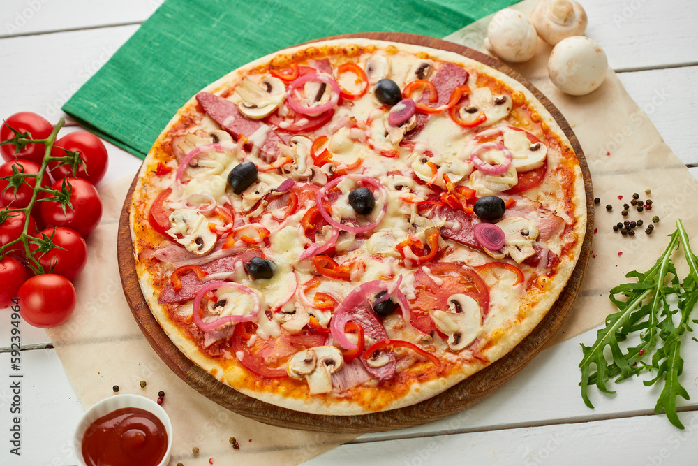 Freshly baked pizza with smoked sausages, red pepper, mushrooms, onion and olives served on wooden background with tomatoes, sauce and herbs. Food delivery concept. Restaurant menu
