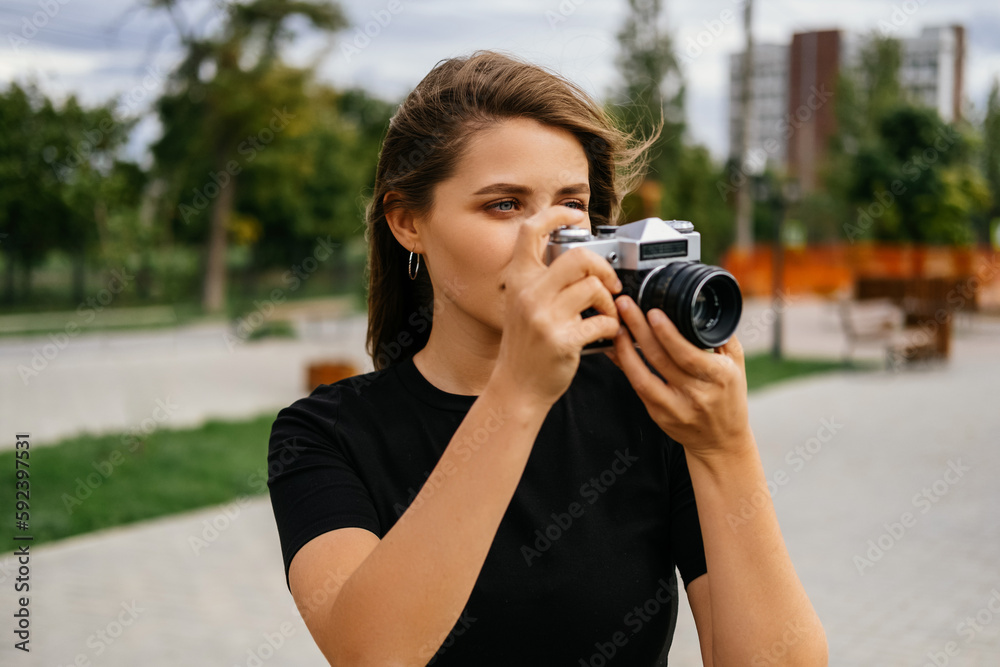 Young blonde woman practices her new hobby outdoors with an old vintage camera.
