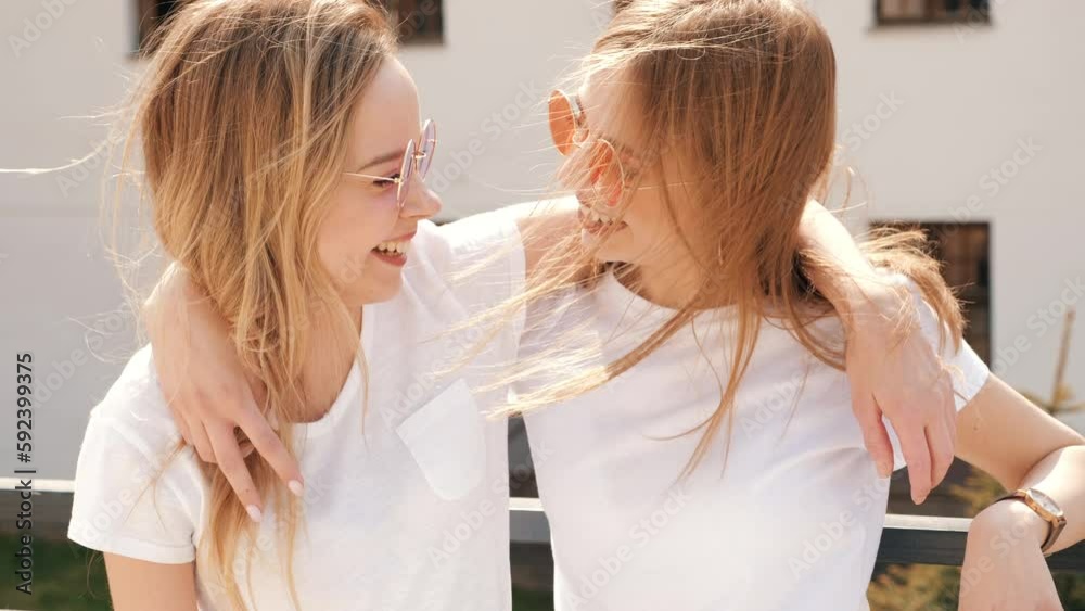 Two young beautiful blond smiling hipster girls in trendy summer clothes. Sexy carefree women posing on street background. Positive models having fun. Showing good relationship. Hugging Two young beautiful blond smiling hipster girls in trendy summer clothes. Sexy carefree women posing on street background. Positive models having fun. Showing good relationship. Hugging