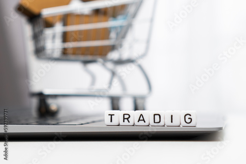 Trading words on cubes laying on the laptop and a toy shopping cart with carton boxes serves as the background.