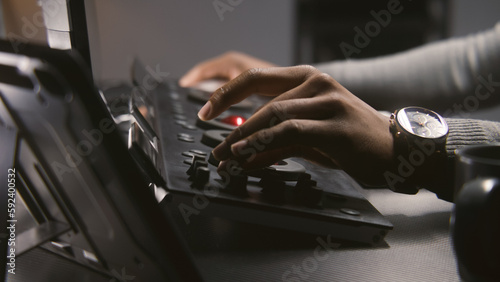 Hands close up of African American colorist working by color grading control panel in studio with modern design. Film editor makes colour correction for video post production. Professional equipment. © Framestock