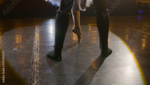 Close up shot of legs of ballet dancers practicing during choreography rehearsal. Man and woman prepare for performance  dance on theater stage illuminated by spotlights. Classical ballet dance art.