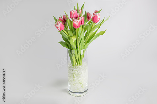 Bouquet of pink tulips in a cylinder glass vase full of hydrogel on white background horizontal