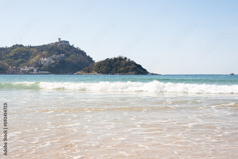 Beautiful beach landscape on a sunny day with clear blue sky and green hills, some waves and sand on the beach. Beautiful beach landscape on a sunny day with clear blue sky and green hills, some waves and sand on the beach.