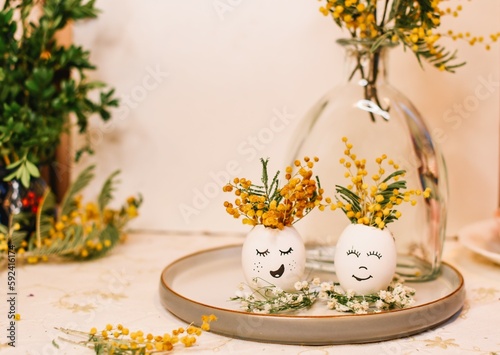 A egg with a face on it sits in a white egg holder with flowers on it.