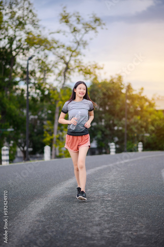 attractive asian woman healthy jogging exercise with transparent plastic water bottle in park outdoor at the evening
