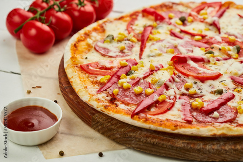 Freshly baked tasty pepperoni pizza with salami, mozzarella cheese, corn and pepper served on wooden background with tomatoes, sauce and herbs. Food delivery concept. Restaurant menu
