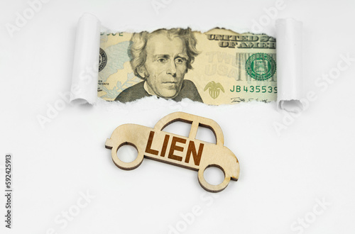 On a white surface in a torn paper window, dollars are next to a wooden model of a car with the inscription - LIEN photo