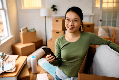Young happy Asian woman moving into new apartment and looking at camera. © Drazen