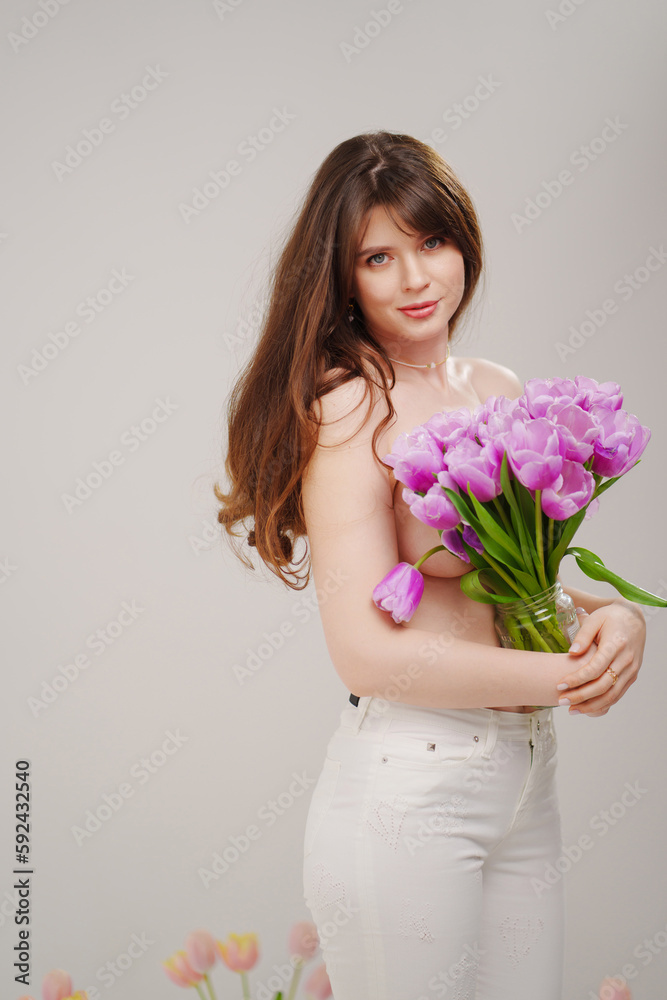 a gentle slim woman topless with tulips on a white background. a gentle slim woman topless with tulips on a white background.