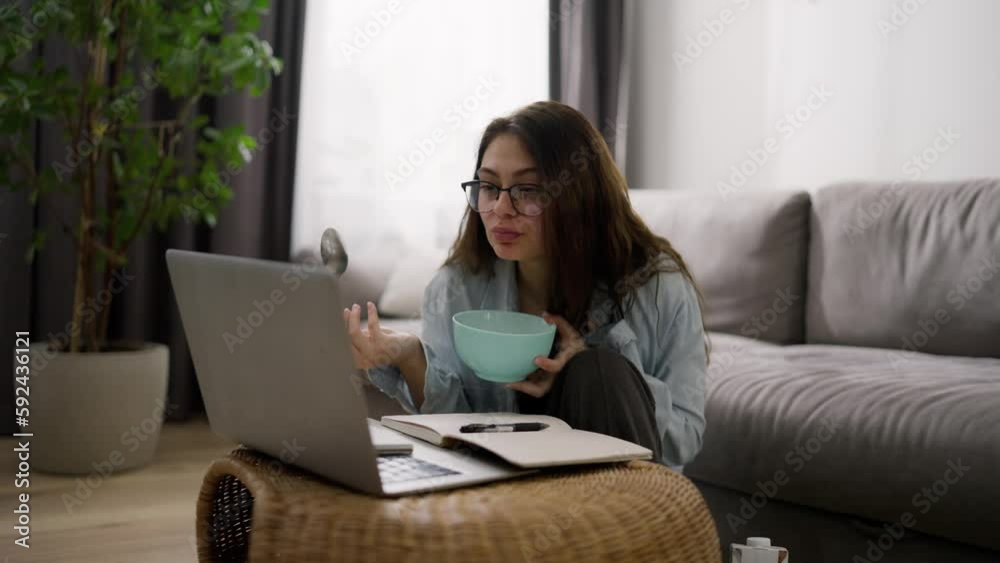 Woman working from home on laptop, making notes and eating cereal in between Woman working from home on laptop, making notes and eating cereal in between