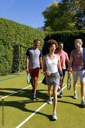Happy diverse group of friends arriving together at tennis court