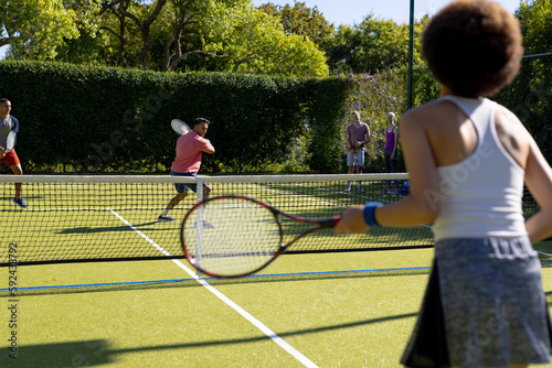 Happy diverse group of friends playing tennis at tennis court